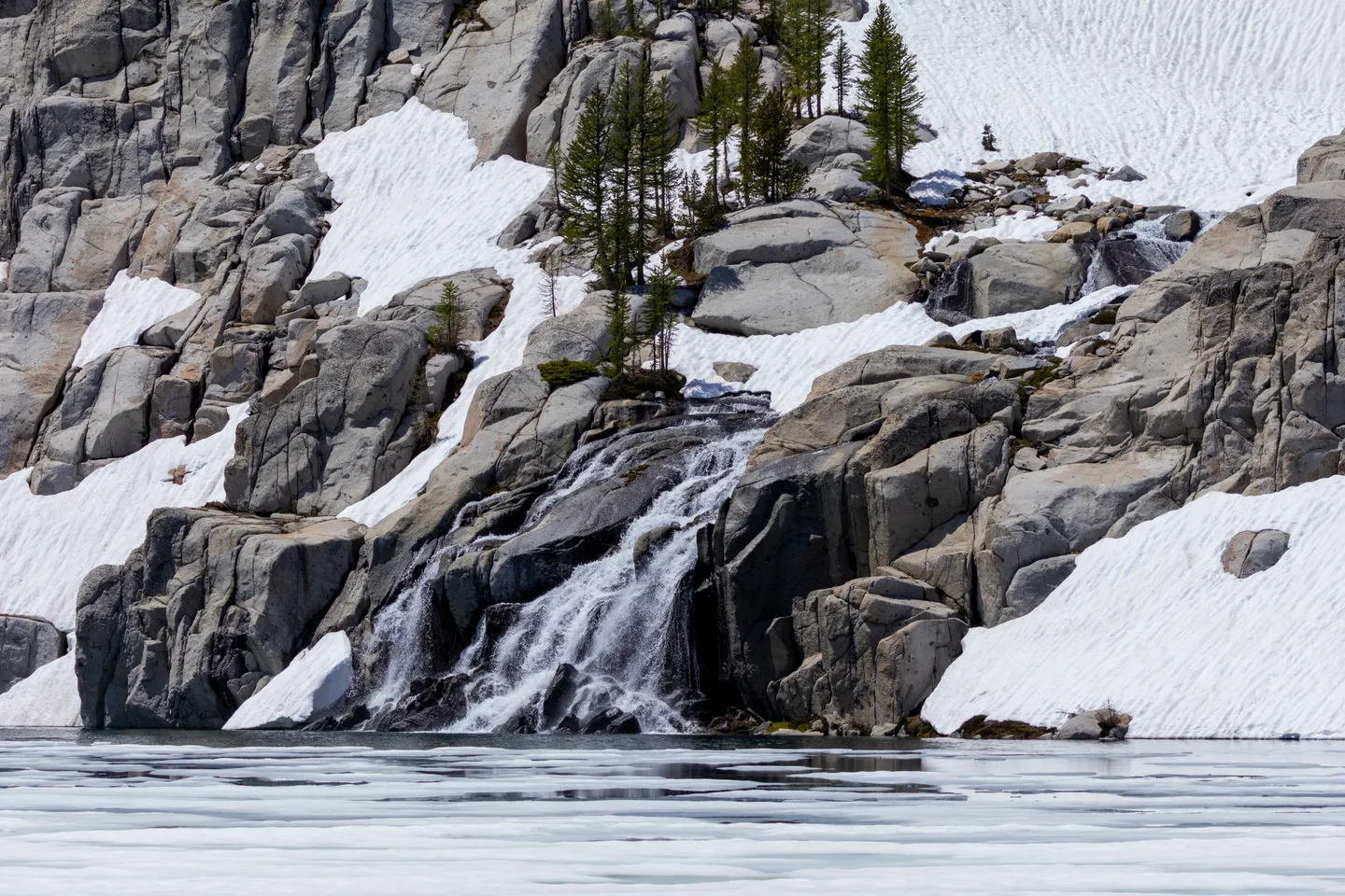 Snowmelt waterfall pouring off granite cliffs into an alpine lake.