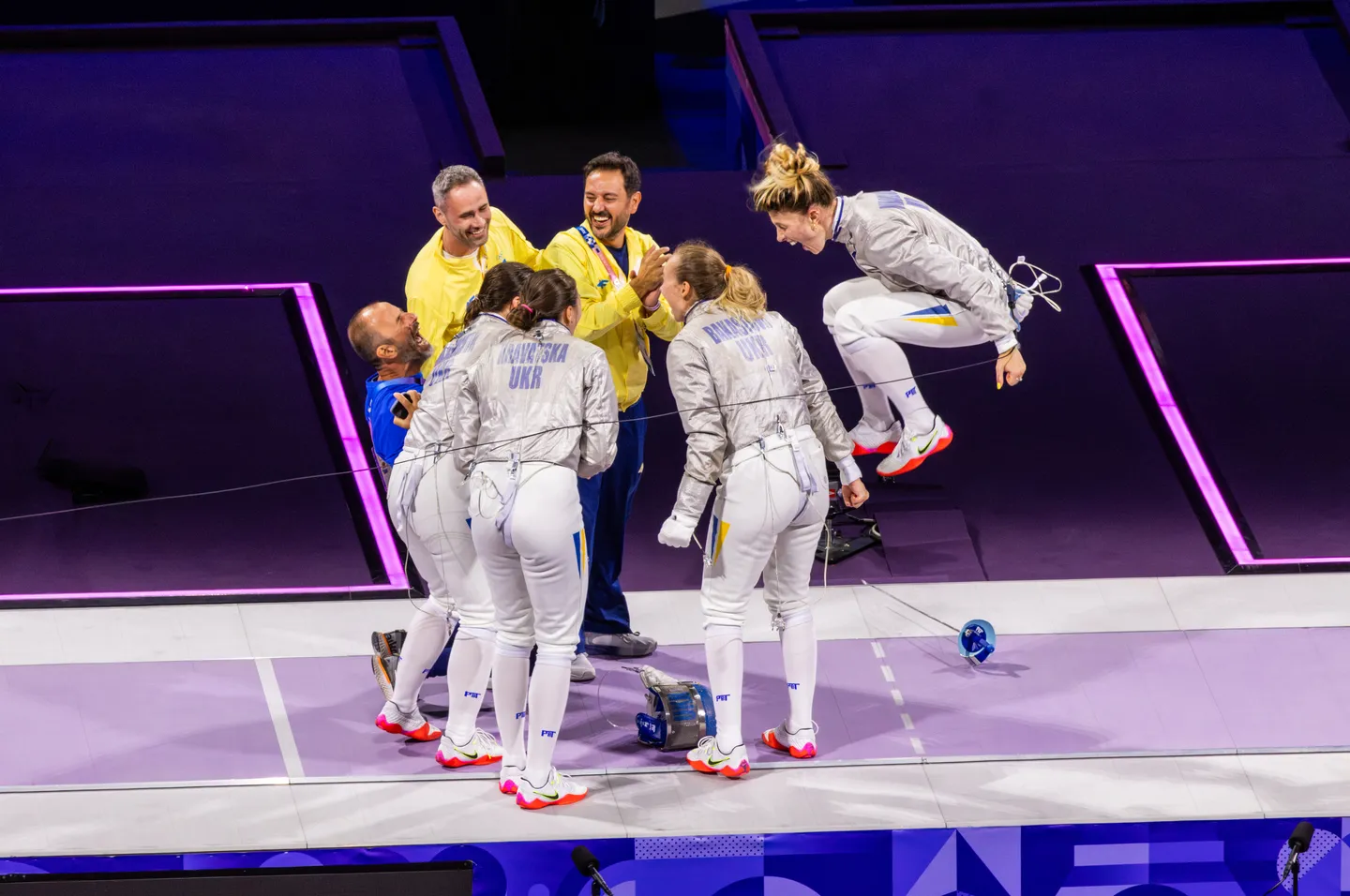 Ukrainian fencers celebrating mid-leap on the piste after a winning bout.